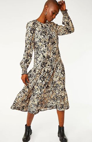 Woman poses with hand to head wearing leopard print tiered midi dress and black shoe boots.