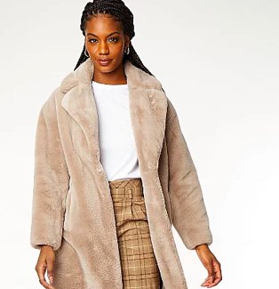 Woman poses wearing open front camel faux fur longline coat over white t-shirt tucked into sand checkered wide-leg trousers.