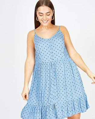 Woman poses smiling wearing blue polka dot print tiered smock sundress.