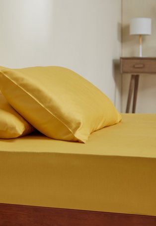 Double bed features yellow fitted sheet and pillowcase with wooden effect desk in the background topped with cream lamp.