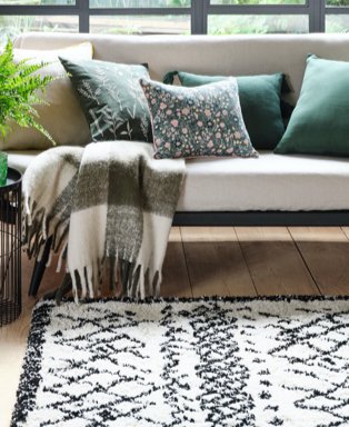 Room features cream sofa topped with green cushions, green checkered throw and homemaker black & white pattern Berber rug.