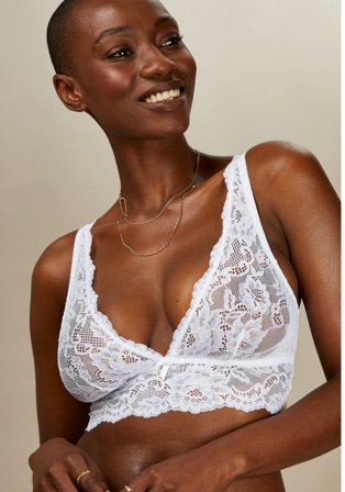 Woman poses smiling wearing white lace bralette.