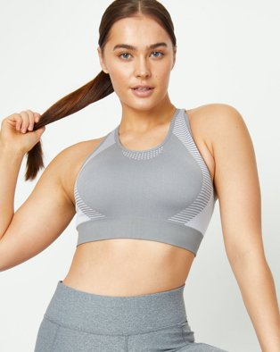 Woman poses holding end of ponytail wearing grey textured sports bra and leggings.