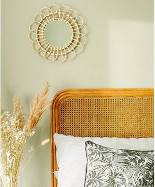 Shot of section of double bed with texured headboard, white and grey floral bedding with large artificial plant and rattan mirror in the background.