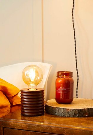 Wooden-effect bedside table features brown ribbed retro lamp and brown candle on tree bark-effect coaster.