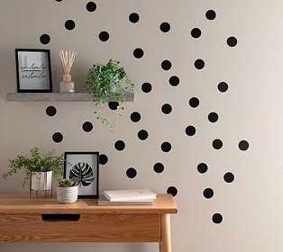 Room with polka dot patterned wall features wooden-effect desk topped with artificial plants, framed print and books, grey shelf features framed print, reed diffuser and artificial plant.