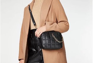 Woman in camel coat, with a camel top, black cross body bag and patent leather skirt.