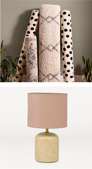 Assortment of abstract patterned rugs leaning against grey wall surrounded by artificial plants. Cream speckled table lamp with pink shade.