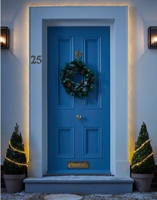 Blue front door surrounded by warm white fairy lights features wreath and potted artificial Christmas trees on either side.