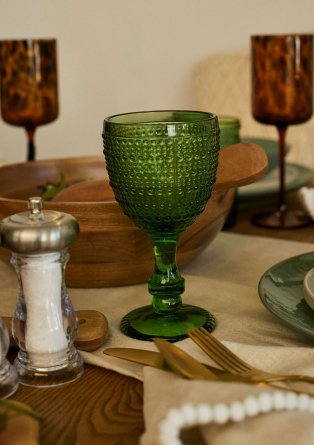 Table setting features green textured wine glass, brown printed glasses and wooden serving dish.