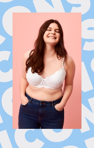Woman smiles with hands in pockets wearing white lace bra and dark blue jeans.