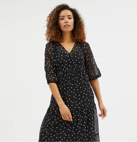 Woman poses wearing black polka dot print mesh tiered midi dress.
