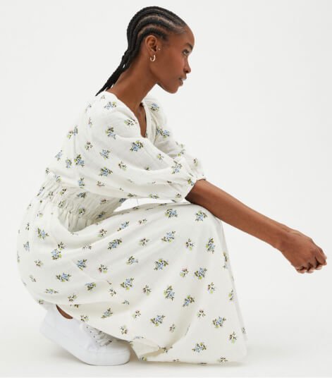 Woman poses side on wearing white floral shirred waist midi dress.