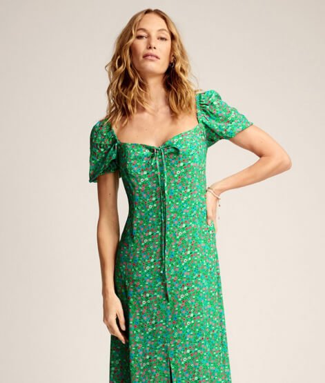 Woman poses with hand on hip wearing green floral midi dress.