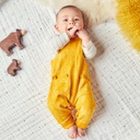 Bird's-eye view of baby lying on bed wearing yellow all in one