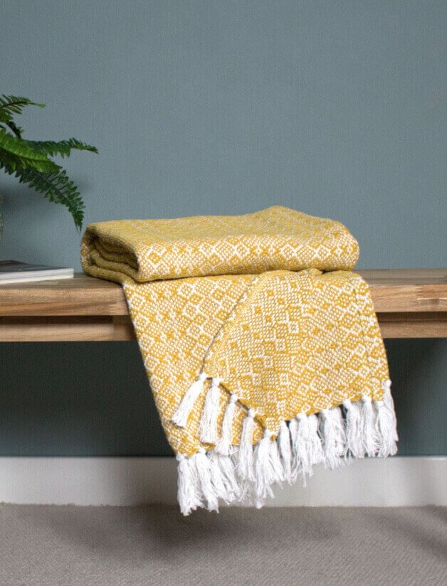 A yellow and white throw folded on a bench.