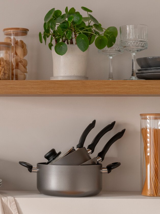 A kitchen counter and shelf, with pans, glasses and a plant on top.