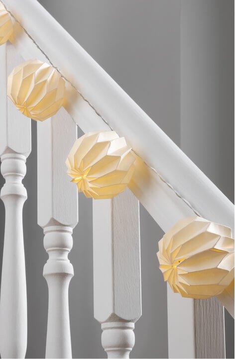 White origami paper string lights draped on a white banister.