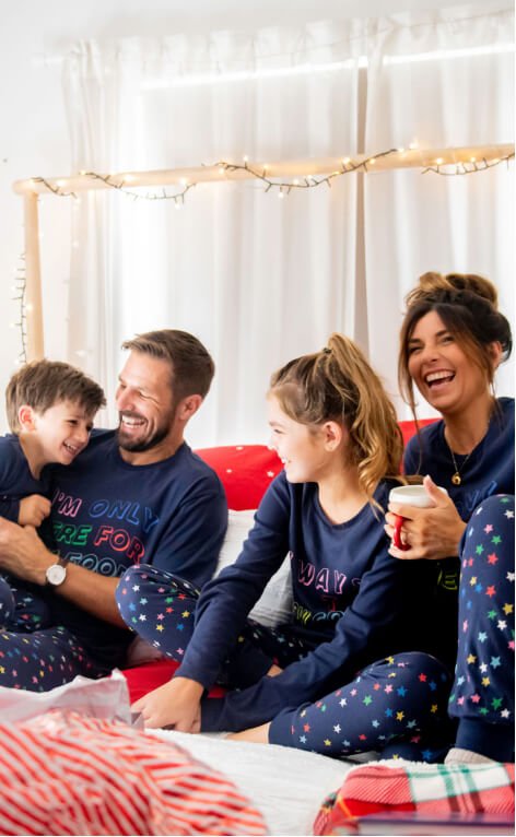 A family of four wearing matching navy pyjamas in bed.