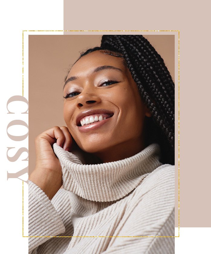 Woman smiles holding collar of light brown ribbed roll neck jumper.