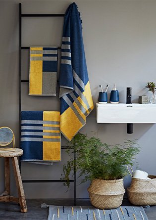 A bathroom with blue, grey and yellow geometric towels hanging from a black towel rail next to a sink with matching toothbrush holder and soap dispensers