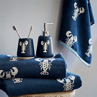 A pile of folded blue and white lobster print towels underneath a toothbrush holder and soap dispenser in a matching pattern