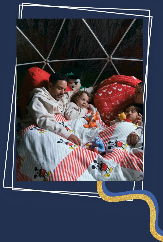 Man and two children lay in Disney Mickey and Minnie Mouse Christmas duvet set surrounded by Disney plush toys.