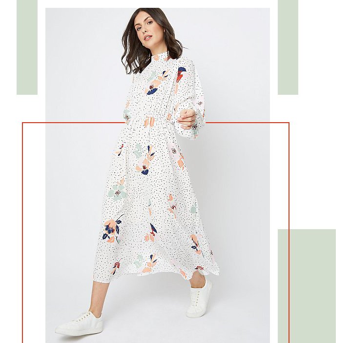 Woman wearing a white long sleeve dress with floral pattern and white trainers