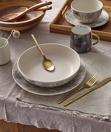 Cream Safari Pattern Dinner Set, Gold-Effect Stainless Steel Cutlery Set, Green Jungle Leopard Pattern Mug, wooden tray, wooden bowl with spoon on wooden table with natural tablecloth and placemats.