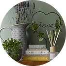 Wooden table topped with three books, natural reed diffuser, grey jug vase, artificial plant and 'love' wire sign with artificial leaves.