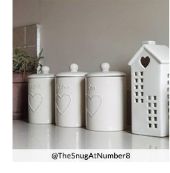 Three white ceramic storage canisters next to a white ceramic house ornament