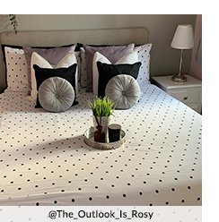 A double bed with a polka dot duvet set, matching grey, black and white cushions and a metal tray with an artificial plant on top