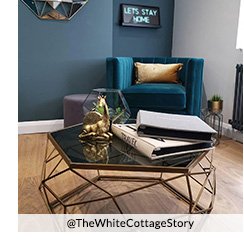 A living room with a geometric copper & glass coffee table decorated with books, a copper giraffe ornament and a glass terrarium, a blue velvet armchair in the corner and a neon sign on the wall