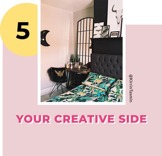 A bedroom with a dark dressing table topped with plants, candles and skincare products next to a double bed with a dark black headboard and a bright tropical print duvet set. 