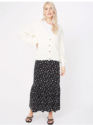 Woman wearing a black and white patterned maxi skirt with a white t-shirt and cream pleated sleeve cardigan