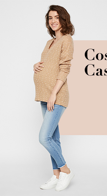 Pregnant woman standing wearing a knitted v neck polka dot jumper, blue jeans and white trainers