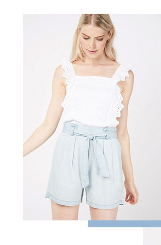 Model wearing a white broderie anglaise crop top with pale blue tie shorts