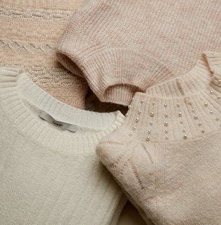 An assortment of natural, cream and light pink folded knitted jumpers.
