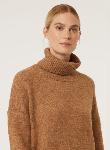 A woman wearing a tan roll neck knitted jumper.