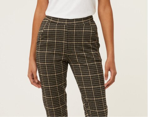 A close shot of a woman wearing checked formal trousers and a white t-shirt.