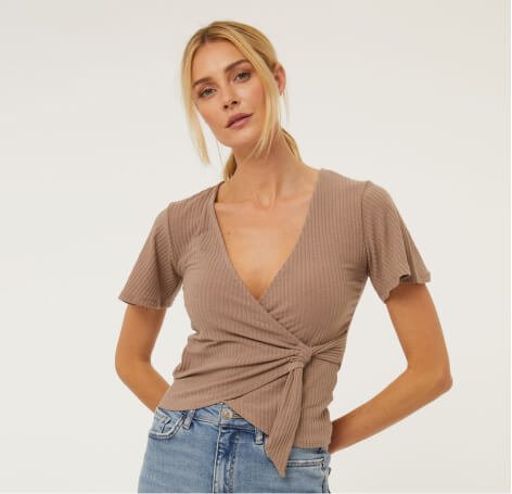 A woman wearing a tan wrap top with jeans.