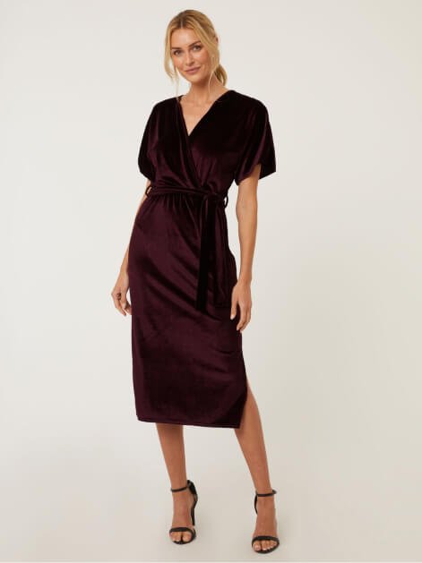 A woman posing in a plum velour wrap dress.