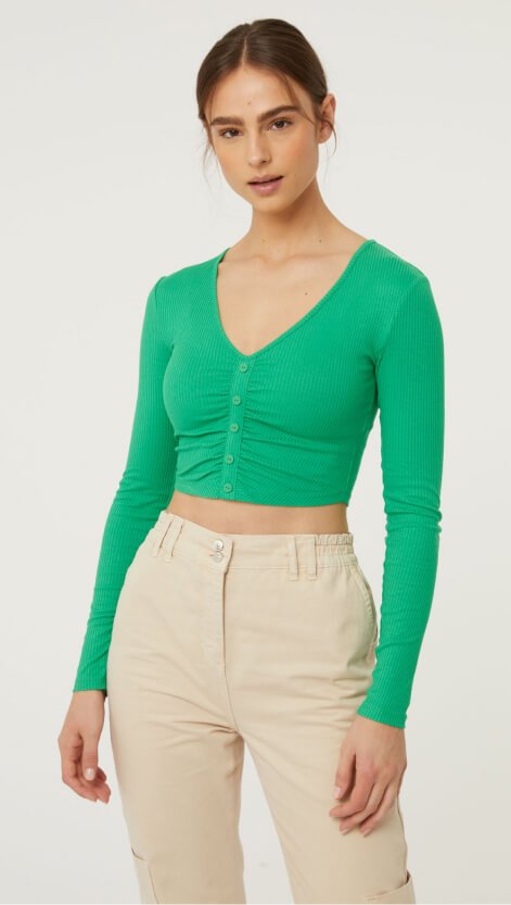 A woman wearing cream trousers and a green cropped top.
