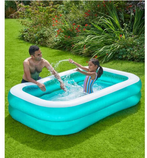 Girl splashes in a paddling pool supervised by male parent.