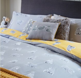 A double bed with a grey and yellow bear print duvet set and matching accent cushions