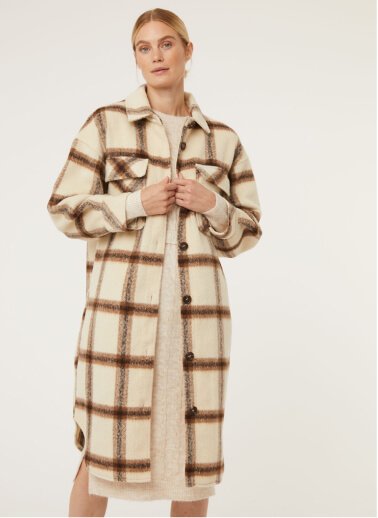A woman wearing a neutral longline checked shacket over a cream knitted dress.