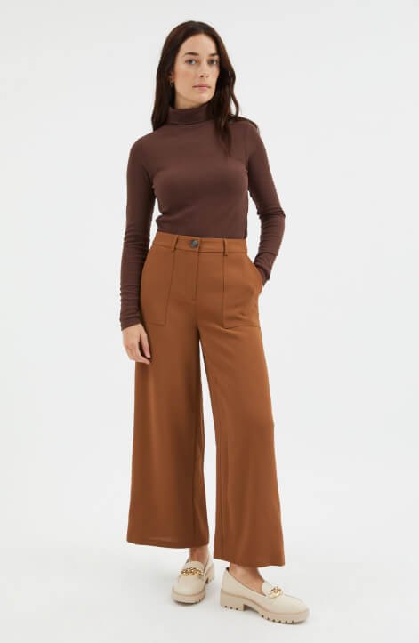 Woman wearing a brown polo jumper and burnt orange trousers.