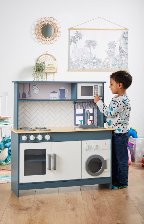 A child playing with a blue and white wooden kitchen.