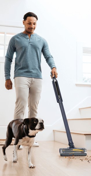 A man using a Shark WandVac pet vacuum cleaner next to his dog.