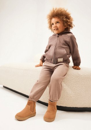 A child wearing a brown hooded top, light brown trousers and camel boots